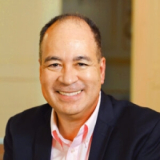 Headshot of a man in a light pink oxford and suit jacket.