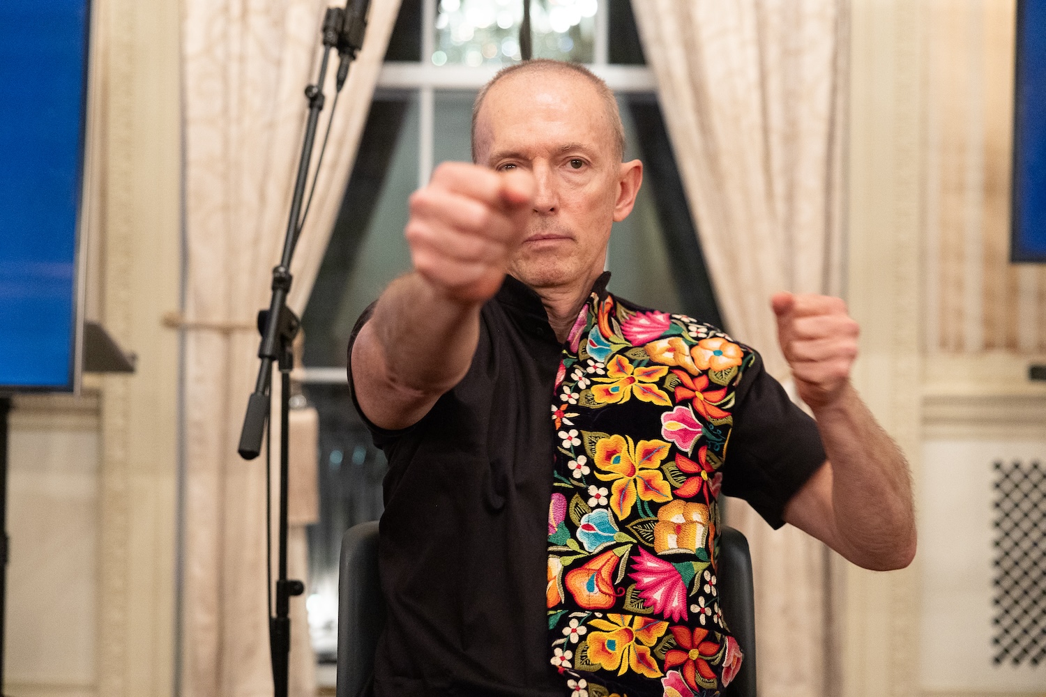 A man in a colorful shirt holds two fists up, one pointed in front of him.