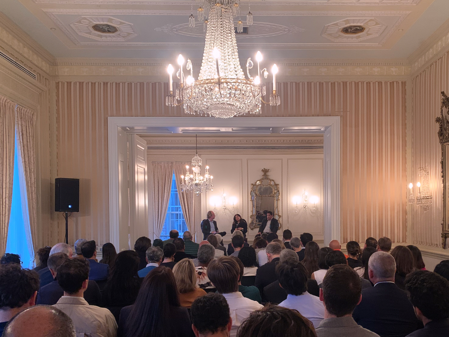 A three-person panel sits in front of a full audience in a ballroom.