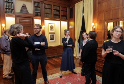 A small crowd mingles in a wood paneled reading room.
